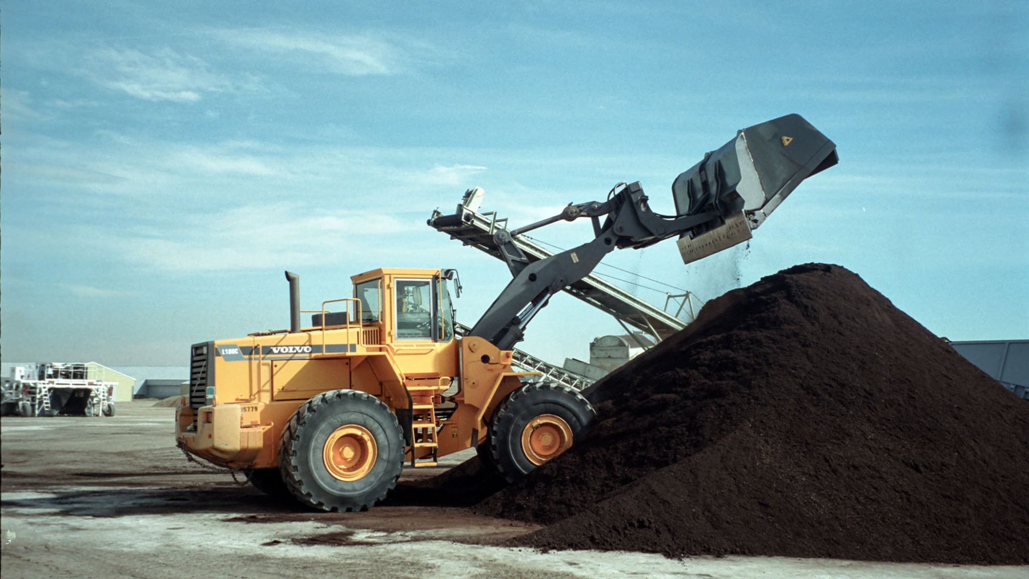 Wheel loader equipped with a Dymax roll out high dump bucket rolling out to dump material with extra dump clearance