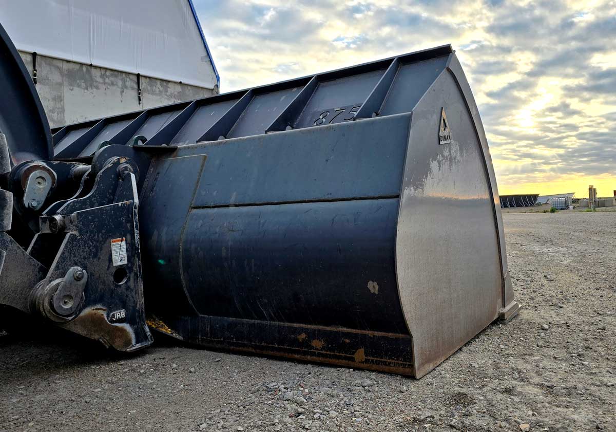 Dymax Light Material Plus bucket on the ground at a farm site at sunset