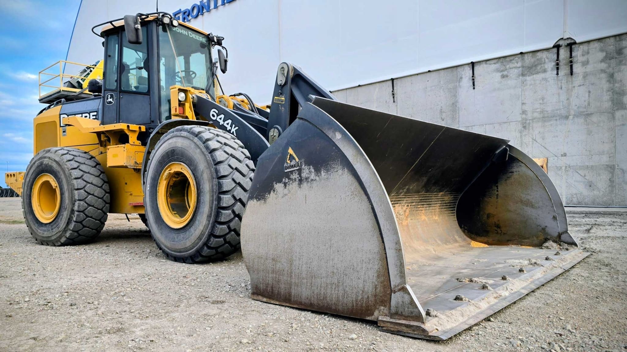 John Deere 644K wheel loader fitted with a Dymax Light Material Plus bucket, parked at a grain co-op