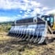 Dozer-mounted rock and root rake removing vegetation, roots, and jobsite debris during land clearing.