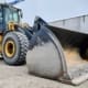 John Deere 644K wheel loader fitted with a Dymax Light Material Plus bucket, parked on gravel beside a concrete wall