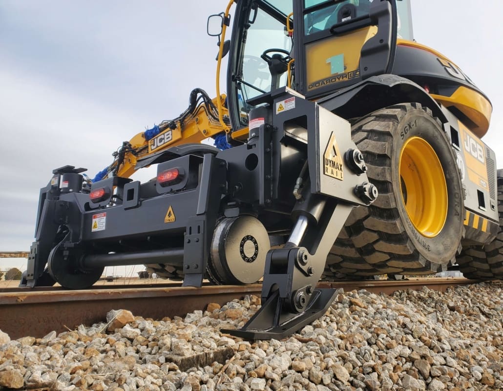 https://dymaxrail.com/ Hi-rail excavator attachment from Dymax Rail operating on railway track with rail guidance wheels