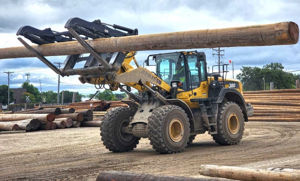 Click to show details - dymax-utility-pole-handling-fork-wheel-loader heel loader handling utility poles with a Dymax pole handling fork attachment